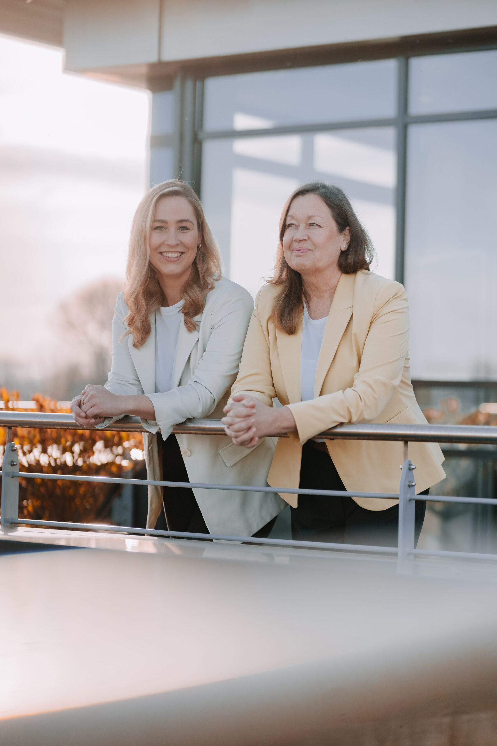 Two employees standing together on a balcony in front of a company building.